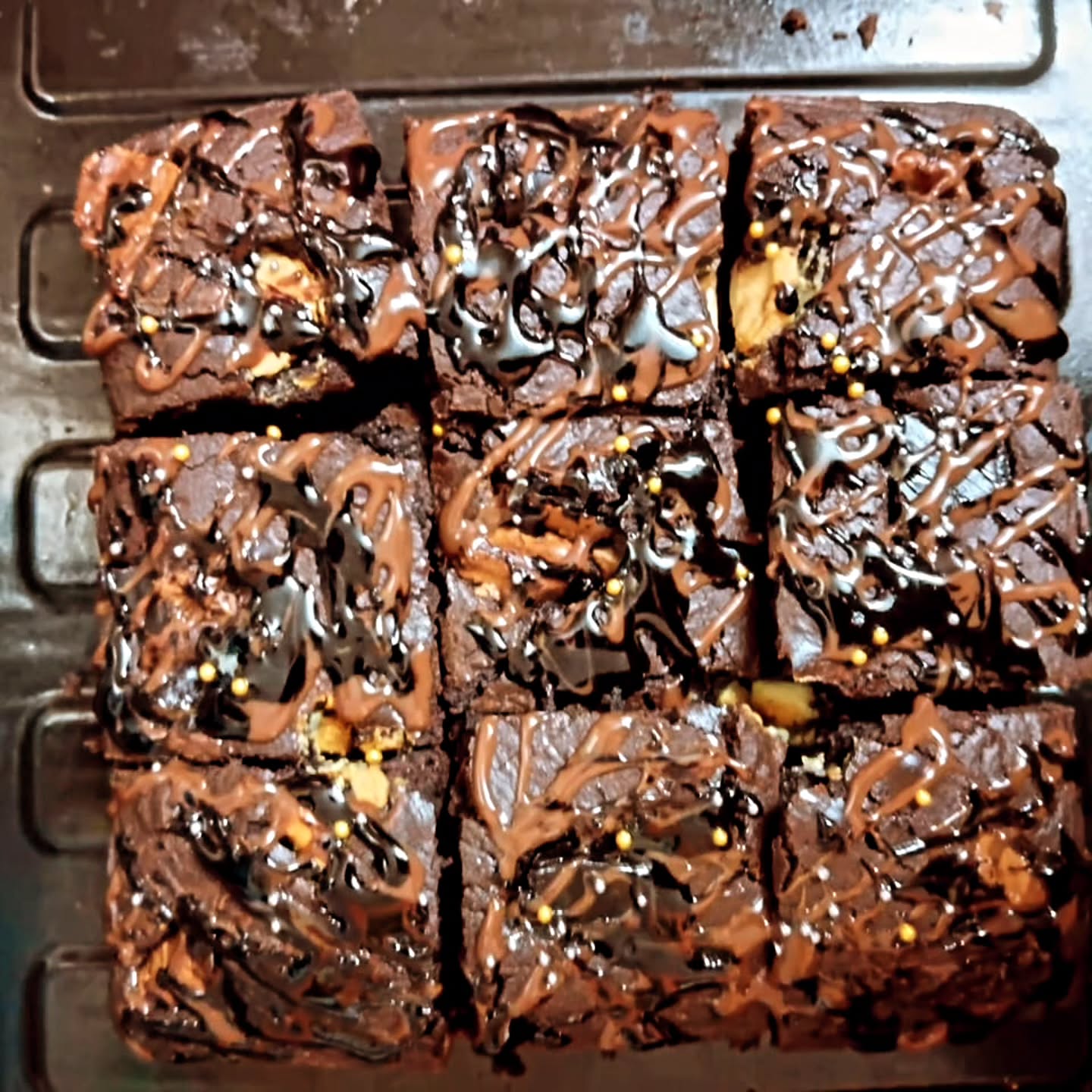 Fresh brownie squares drizzled with chocolate on a cooling rack